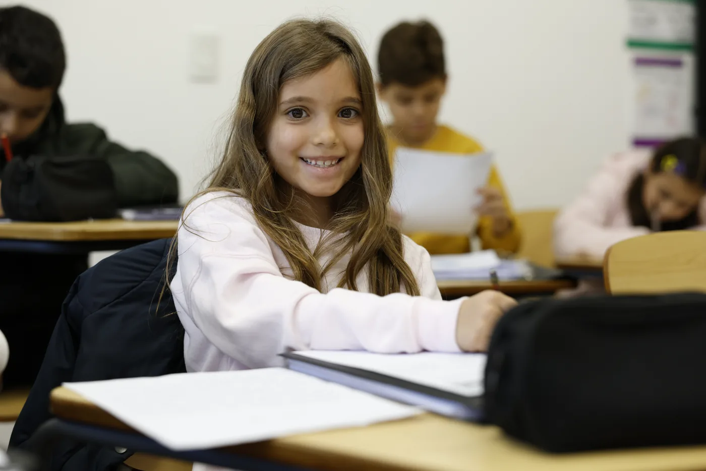 Aluna da Global Me School sorrindo em sala de aula, com colegas ao fundo