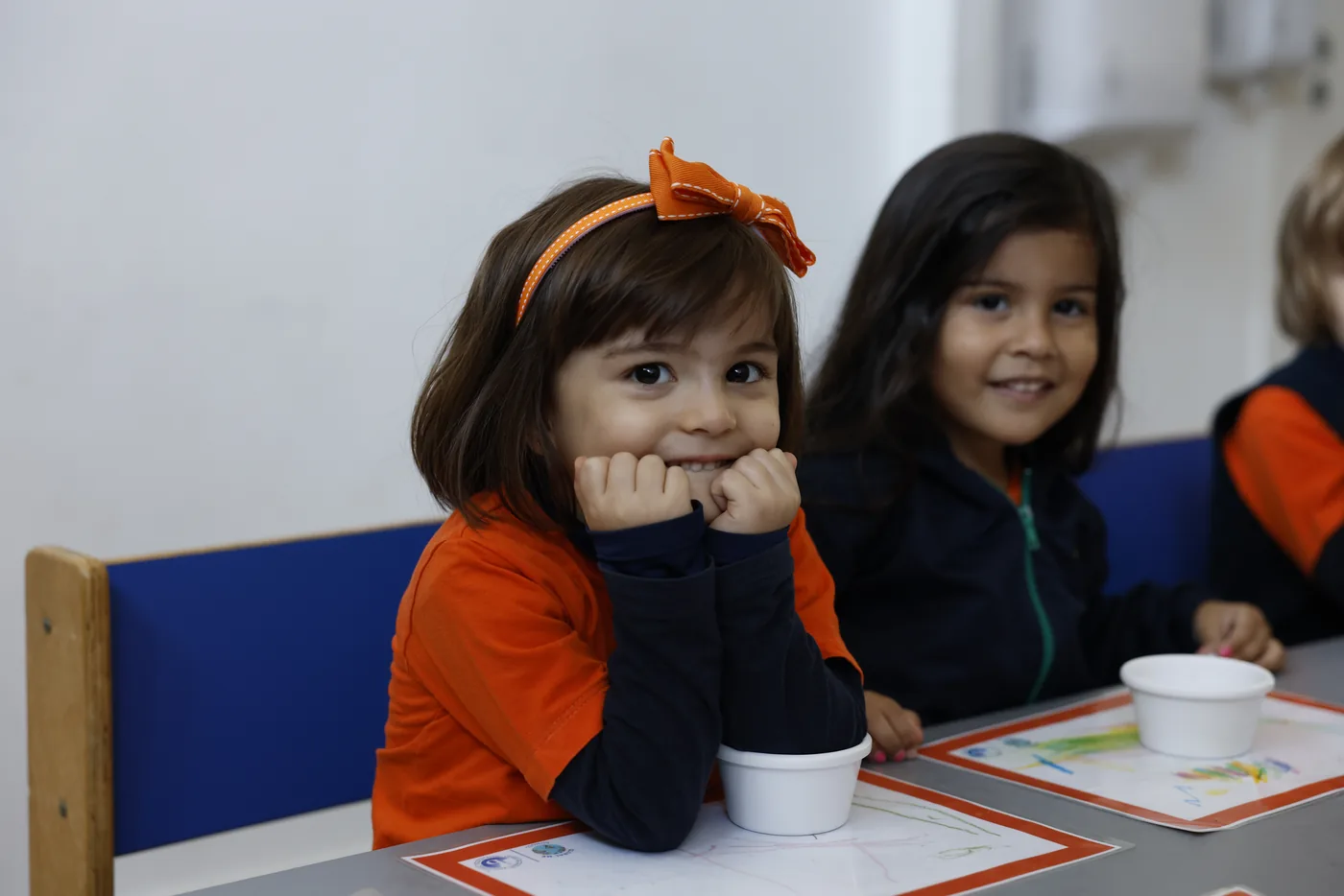 Criança da Global Me School sorrindo na sala de aula, com uma amiga ao lado